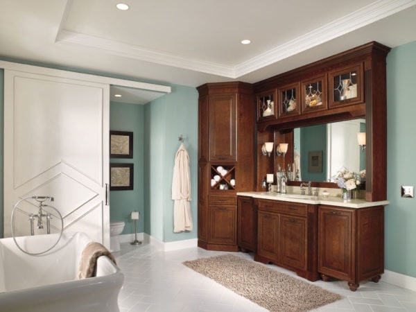Bathroom design with built-in vanity and stained wood cabinets, vintage tub and recessed lighting