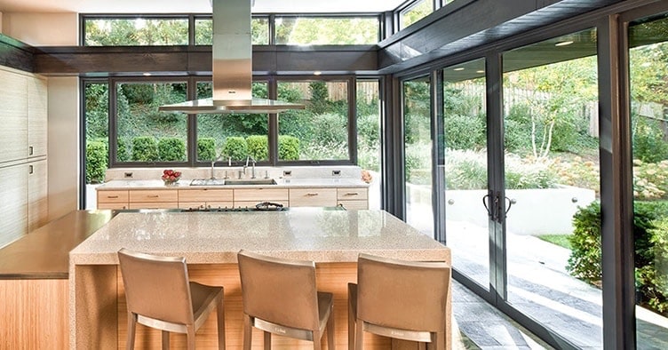 A large kitchen blends glass walls and windows with swinging French doors for a magnificent view